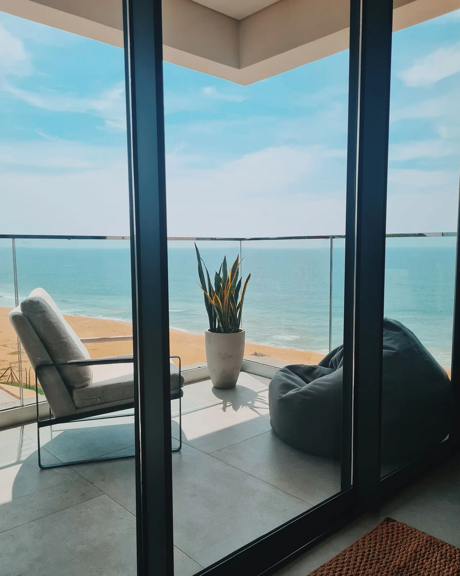 Balcony with a lounge chair and a potted plant looking straight out over a sandy beach and the sea