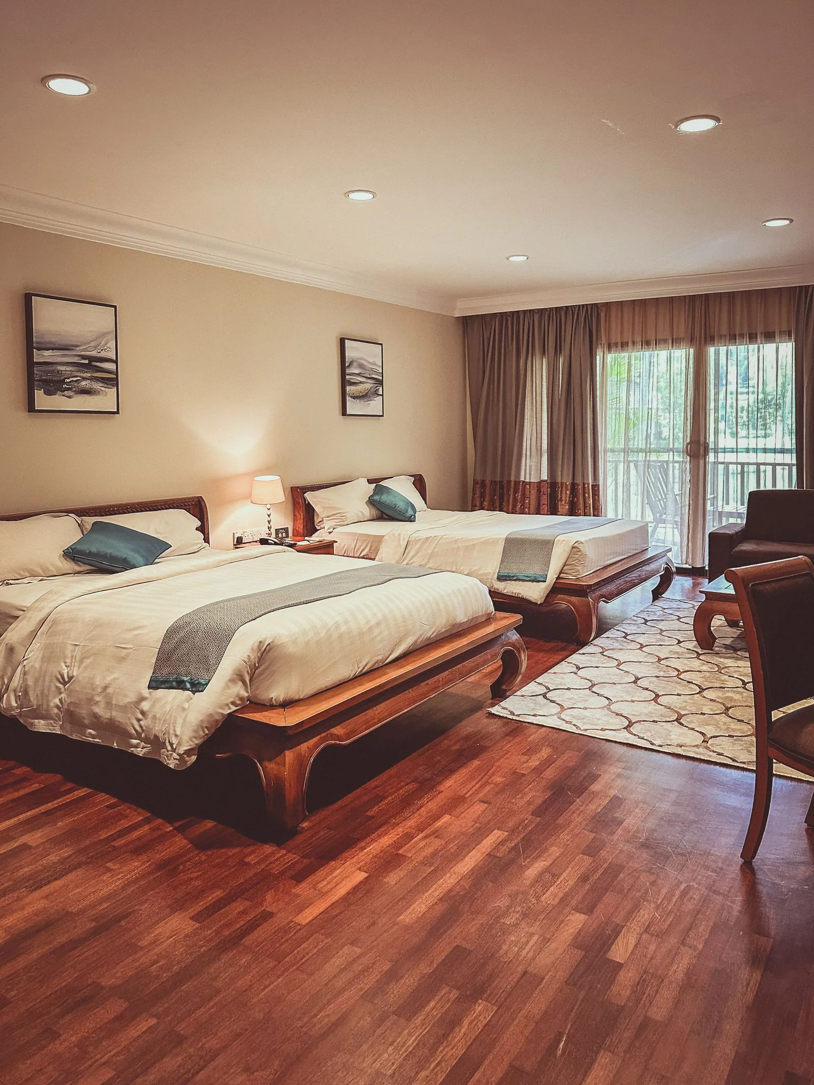 Spacious room with two double beds side by side, a wooden floor and a window onto greenery