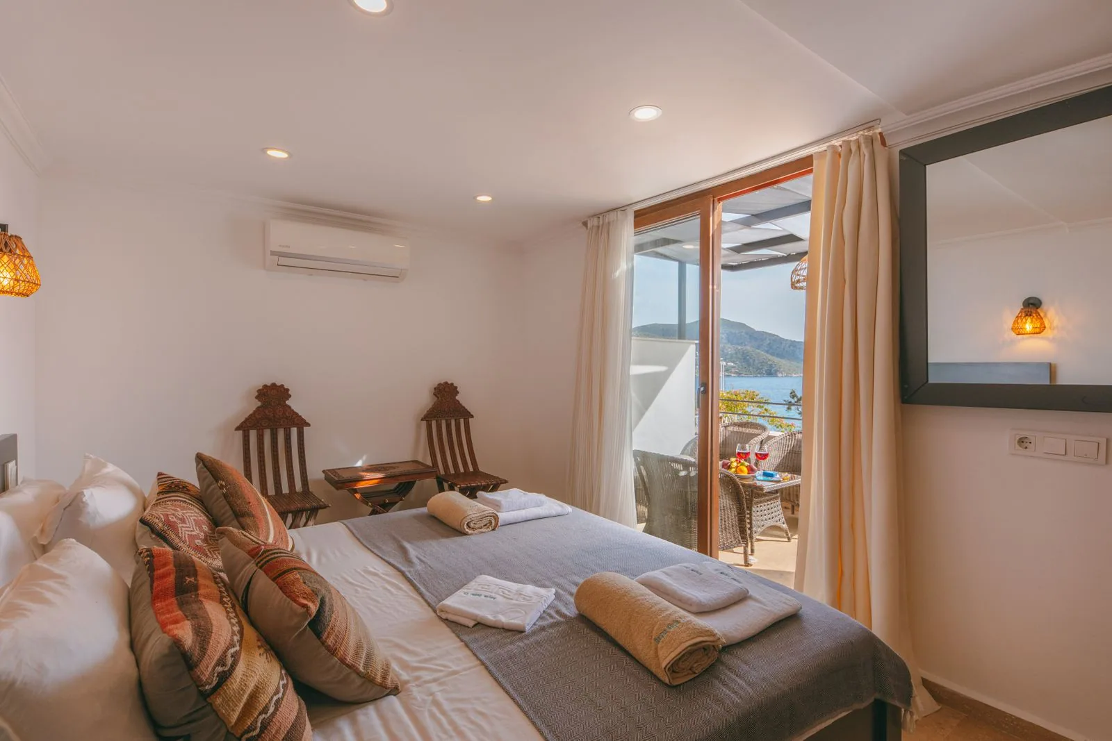 Guest room with a bed facing glass doors that open onto a balcony and the sea beyond
