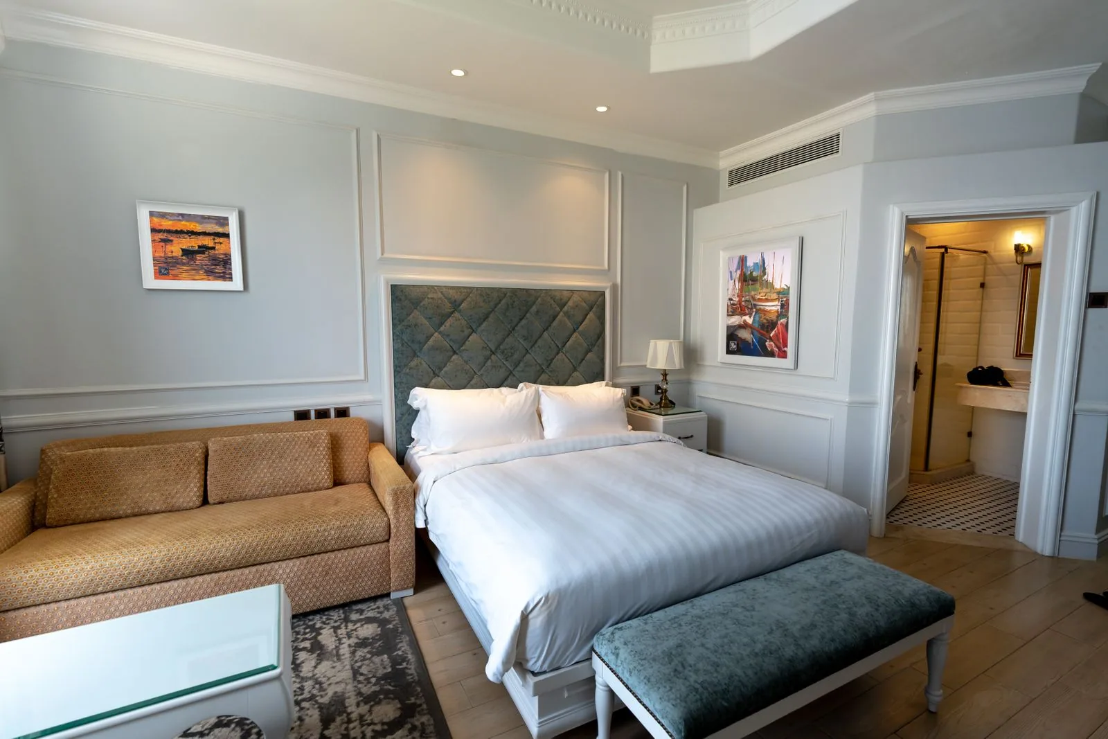 Light grey room with a double bed, a long sofa and an open door to the bathroom
