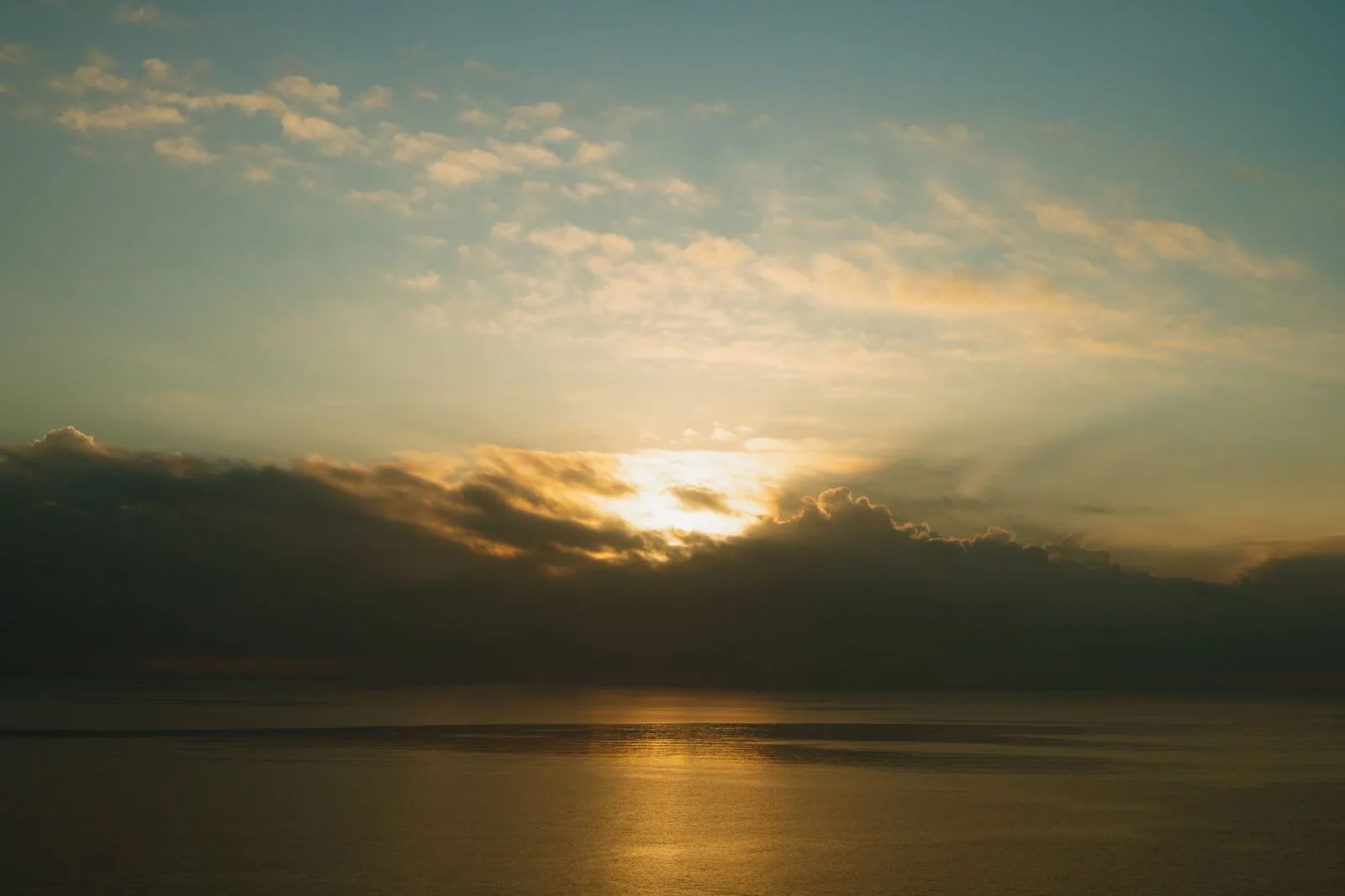 Early sunlight breaking through clouds above a still, grey sea